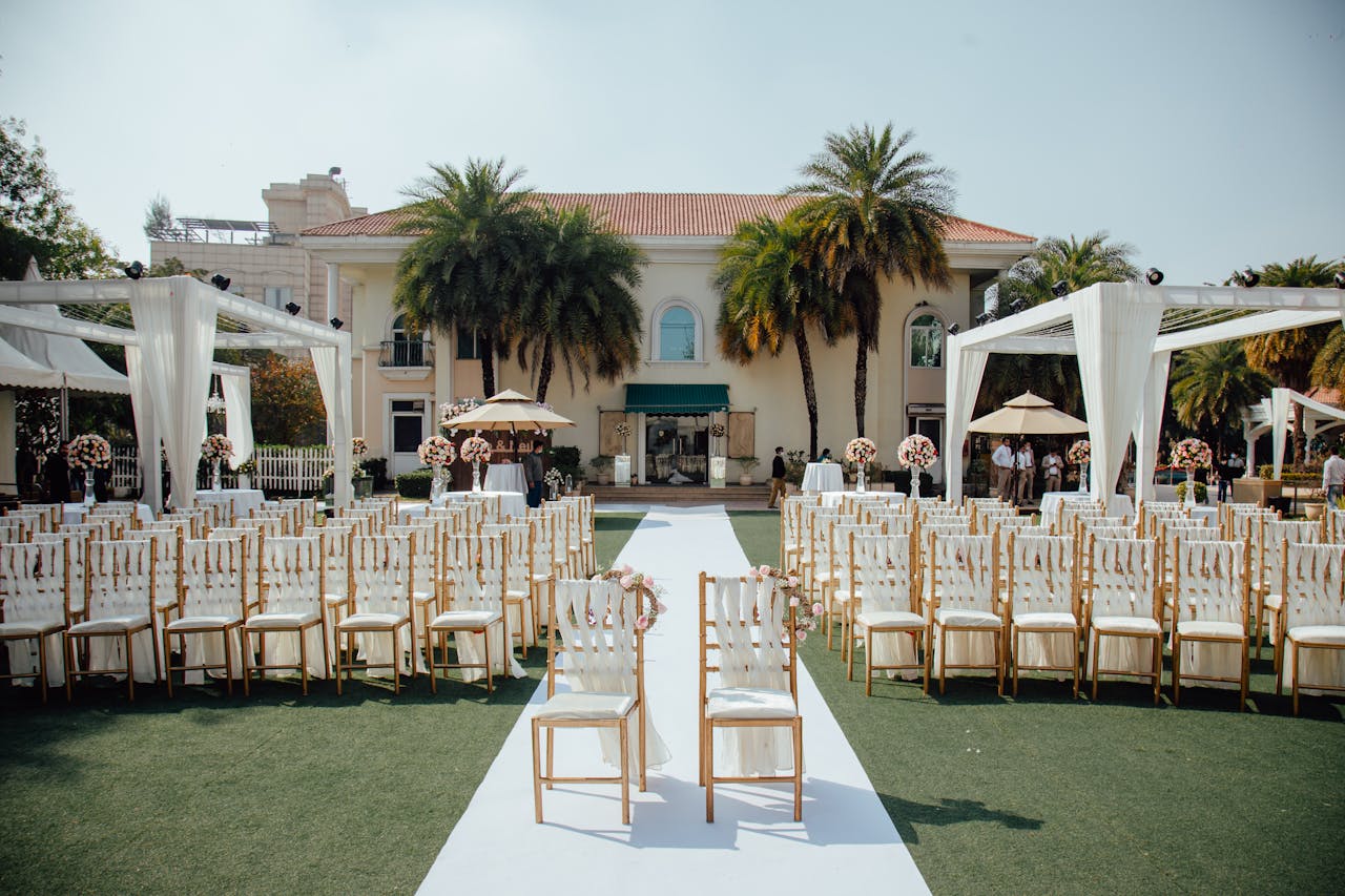 about-us Beautiful outdoor wedding ceremony setup with rows of decorated chairs facing a luxurious villa.